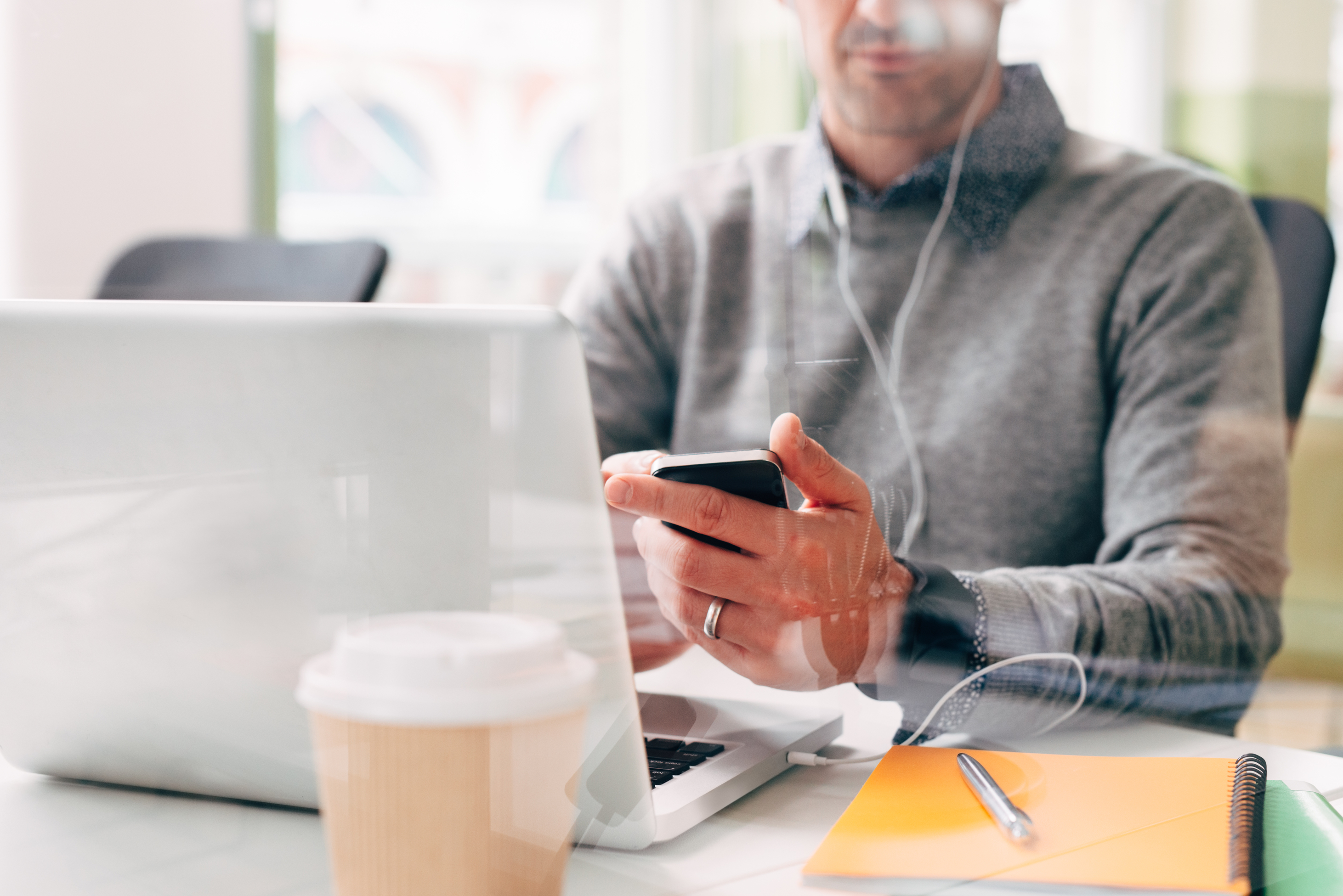 Man working on laptop and looking at phone